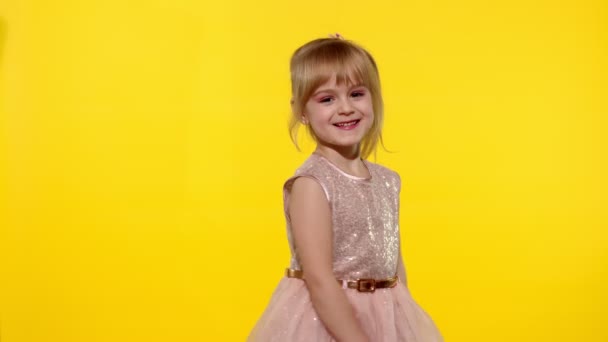 Hola o adiós. Niña pequeña niña rubia sonriente saludando con la mano sobre fondo amarillo — Vídeo de stock