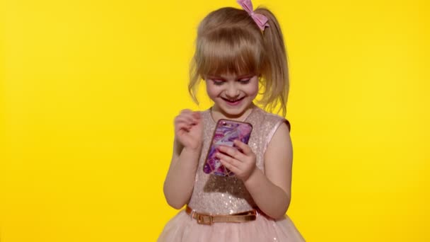Κορίτσι παιδί με φόρεμα χρησιμοποιώντας το κινητό τηλέφωνο, ανακάλυψε μεγάλη νίκη ειδήσεις. Παιδί κάνει χειρονομία νικητής — Αρχείο Βίντεο