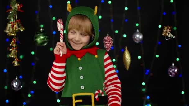 Noel Baba yardımcısı Noel Baba kostümlü çocuk lolipop şekerli neşeli gülümsemeli. — Stok video