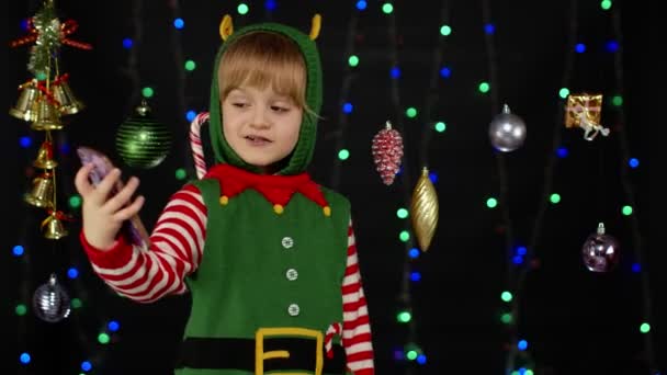 Ребенок девочка в костюме помощника эльфа Санта-Клауса делает видеозвонок на мобильный телефон — стоковое видео