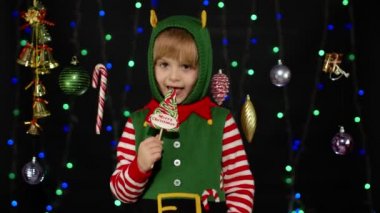 Noel 'de elf Noel Baba yardımcı kostümlü çocuk lolipop şekerleri yalıyor.