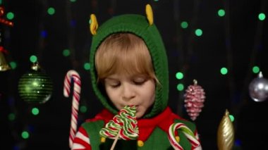 Noel 'de elf Noel Baba yardımcı kostümlü çocuk lolipop şekerleri yalıyor.