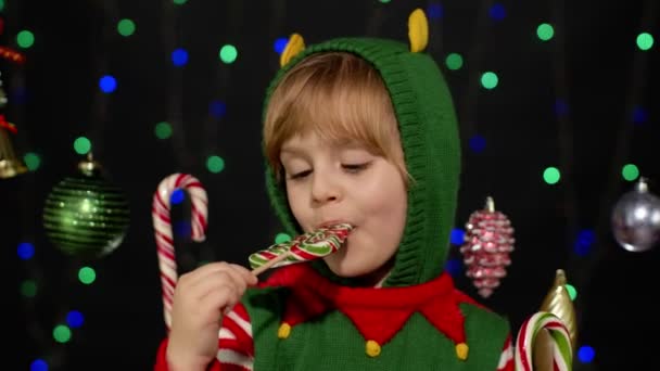Child kid girl in Christmas elf Santa Claus helper costume licking candy lollipop caramel sweets — Stock Video