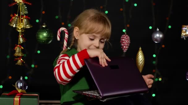 Παιδί κορίτσι στο κοστούμι ξωτικό των Χριστουγέννων κάνει ψώνια σε απευθείας σύνδεση χρησιμοποιώντας φορητό υπολογιστή, περιήγηση στα μέσα κοινωνικής δικτύωσης — Αρχείο Βίντεο