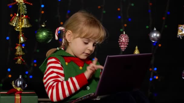 Menina criança em traje de duende de Natal fazendo compras on-line usando laptop, navegando nas mídias sociais — Vídeo de Stock