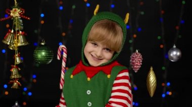 Noel Elf Noel Baba yardımcı kostümü giyen genç kız siyah arka planda baş parmak gösteriyor.