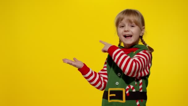Menina criança no elfo de Natal Santa ajudante traje aponta dedos no espaço em branco mostra área de publicidade — Vídeo de Stock