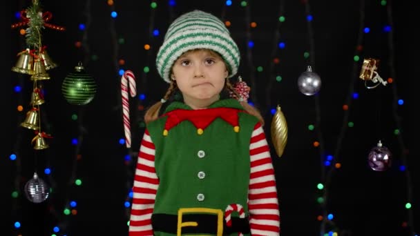 Blyg skam barn flicka i jul tomte hjälpreda kostym poserar ser kamera gör roliga ansikten — Stockvideo