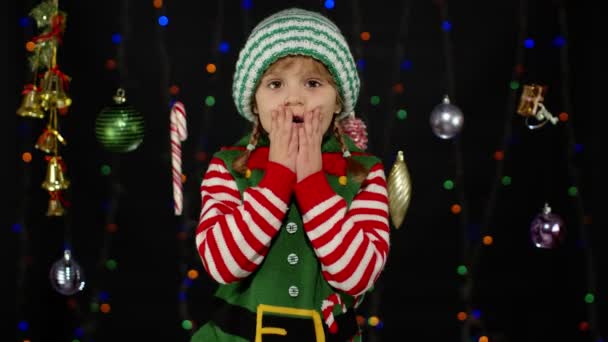 Dziecko dziewczyna w Boże Narodzenie elf Święty Mikołaj pomocnik kostium. Dziecko robi gest zwycięzcy, macha rękami — Wideo stockowe