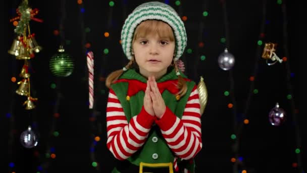 Karácsonyi manó jelmezes gyerek könyörög, újévi ajándékokért imádkozik. Együtt tartja a tenyerét. — Stock videók