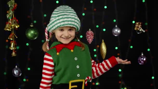 Дитяча дівчинка в різдвяному ельфі Санта помічник костюм точка з рукою в порожньому просторі показує рекламну зону — стокове відео