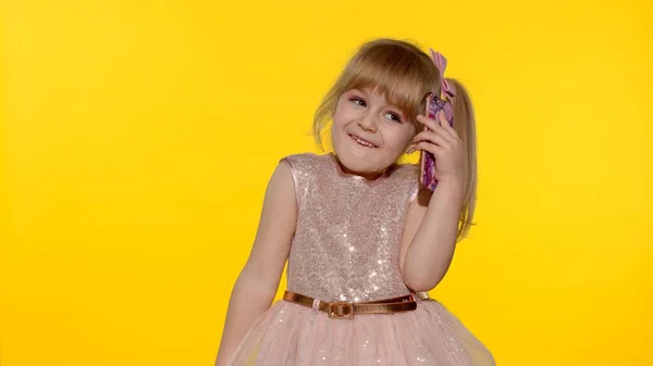 5-6 yaşlarındaki gülümseyen kız sarı arka planda cep telefonuyla konuşuyor. — Stok fotoğraf