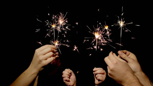 Close-up of hands holding and waving bengal fire burning sparklers in front of black background — Stock Photo, Image