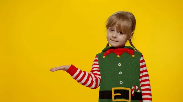 Дитяча дівчинка в різдвяному ельфі Санта помічник костюм вказує пальці в порожньому просторі показує рекламну зону — стокове фото