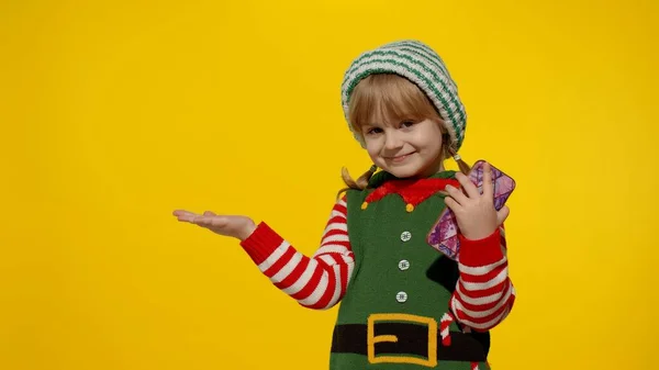 Menina criança com telefone celular no elfo de Natal Santa ajudante traje aponta os dedos de lado na parede em branco — Fotografia de Stock