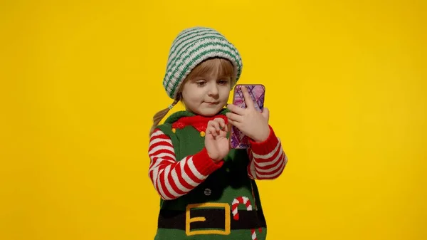 Маленька дівчинка з різдвяного ельфа Санта Клаус костюм помічника робить відео дзвінок на мобільному телефоні — стокове фото