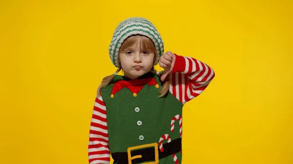Menina criança displesed no elfo de Natal traje de Papai Noel ajuda mantém o polegar para baixo e mostra gesto de antipatia — Fotografia de Stock