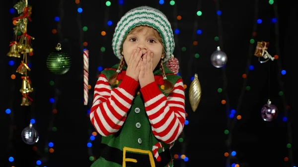 Девочка в костюме помощника рождественского эльфа Санта Клауса смотрит в камеру и делает большой рот, закрывающий глаза. — стоковое фото