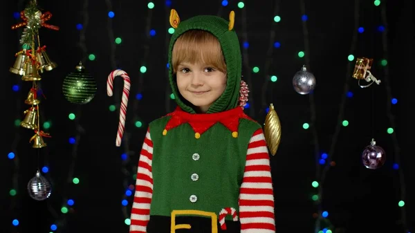Сором'язлива дівчинка сором'язлива в костюмі різдвяного ельфа Санта-помічника позує на камеру і посміхається — стокове фото