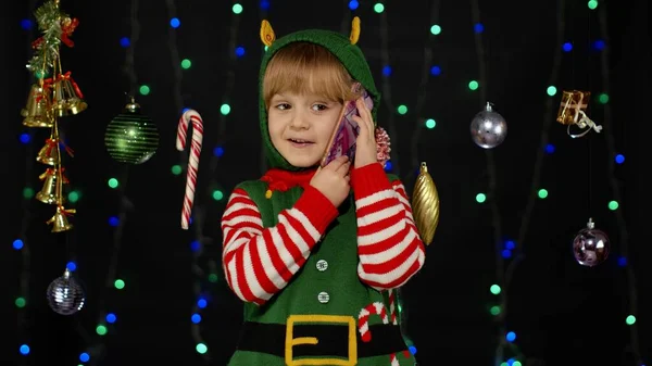 Menina criança no elfo de Natal Santa Claus traje auxiliar fazendo chamadas de parabéns no telefone móvel — Fotografia de Stock