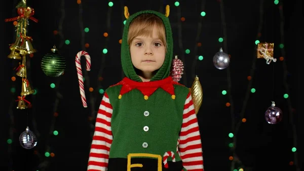Сором'язлива дівчинка сором'язлива в костюмі різдвяного ельфа Санта помічника позує, дивлячись камеру, роблячи смішні обличчя — стокове фото