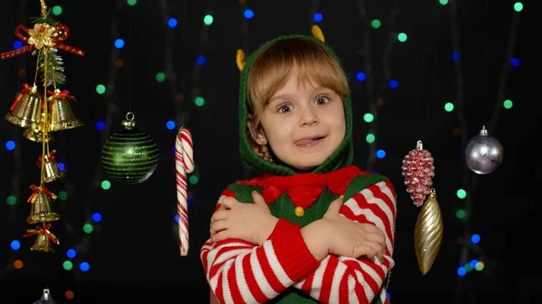 Menina loira criança no elfo de Natal Santa traje auxiliar mostrando língua, flertando, abraçando, abraçando — Fotografia de Stock