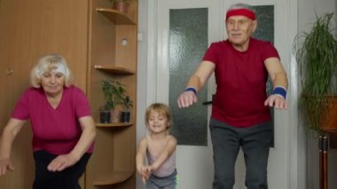 Torunu olan yaşlı çift evde spor yapıyor, antrenman yapıyor, spor yapıyor, spor yapıyor.