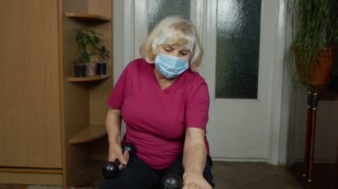 Spor kıyafetleri içinde halter kaldıran yaşlı büyükanne kadın evde halter egzersizi yapıyor.