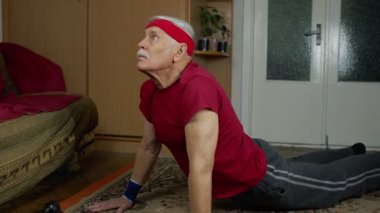 Oturma odasında spor giyim bölümünde yaşlı, beyaz bir adam sabahları evde şınav çekiyor.