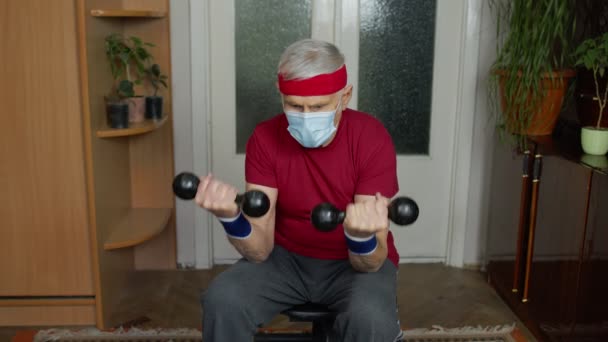 Starszy Dojrzały dziadek mężczyzna w sportowe odzież robi ciężarów hantle ćwiczenia w domu — Wideo stockowe