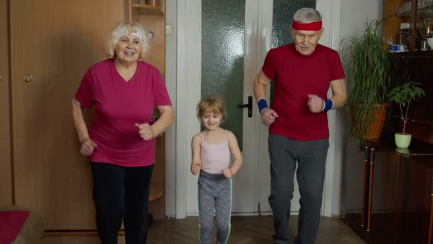 スポーツウェアの孫娘と成熟した祖父母は、自宅でスポーツジョギングワークアウトの演習を作る — ストック動画