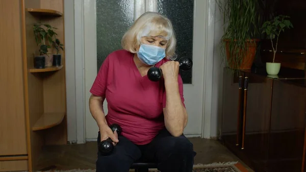 Anziana donna caucasica anziana che fa pesi manubri di sollevamento esercizio a casa durante il coronavirus — Foto Stock
