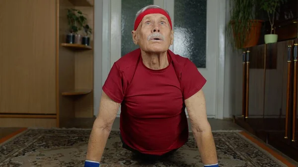 Senior homme caucasien âgé en vêtements de sport dans le salon, faire matin push-up exercice à la maison — Photo