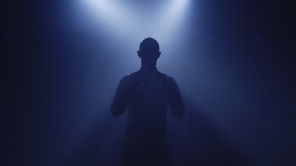 Backlit σιλουέτα του DJ άνθρωπος στέκεται στο σκοτεινό ντίσκο νυχτερινό κέντρο διασκέδασης, βάζοντας ακουστικά για να ακούσετε μουσική — Αρχείο Βίντεο
