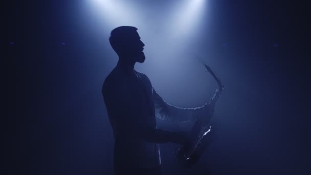 Bakgrundsbelyst siluett av saxofonist man med saxofon i mörk nattklubb studio och börja spela sax — Stockvideo
