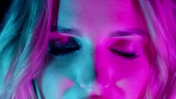 Sensual menina loira emocional com maquiagem brilhante abrindo lentamente os olhos em luzes de néon verde rosa — Vídeo de Stock