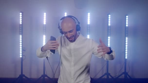 Performance DJ live d'un homme chauve énergique avec écouteurs, dansant en écoutant de la musique depuis un téléphone portable — Video