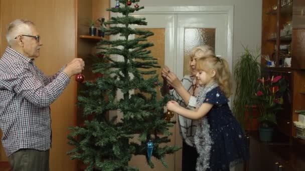 Enfant fille avec grand-mère aînée et grand-père décorer arbre de Noël artificiel avec des jouets — Video