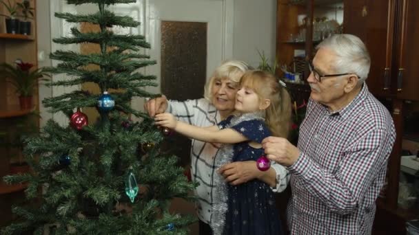 Menina com avós seniores família decoração árvore de Natal artificial, feriados de Ano Novo — Vídeo de Stock