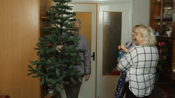 Children girl kid with elderly couple grandfather, grandmother decorating artificial Christmas tree — Stock Video