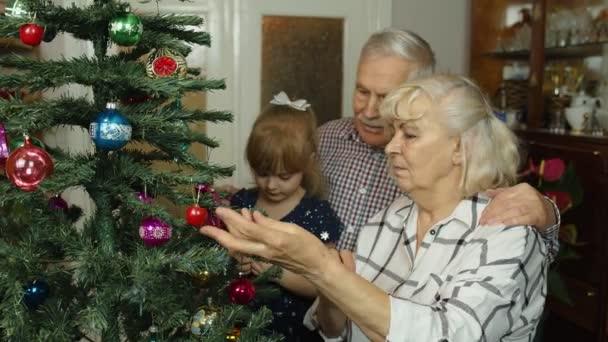 Anak perempuan dengan nenek senior, kakek menghias pohon Natal buatan dengan ornamen dan mainan — Stok Video