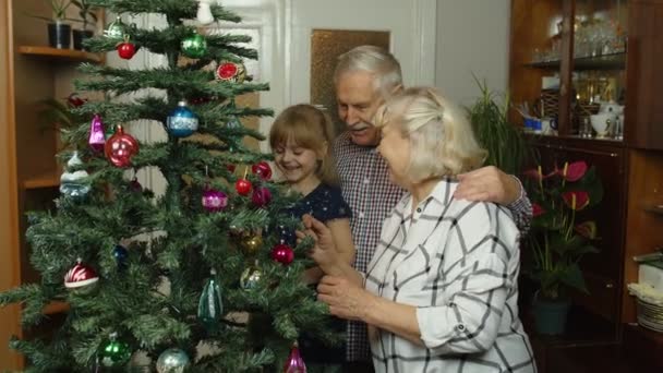 Dzieci dziewczyna z dziadkami w podeszłym wieku dekorowanie sztucznej choinki w domu — Wideo stockowe