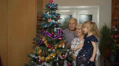 Büyükbaba, büyükanne ve torun. Çocuk yapay Noel ağacına çelenk yakıyor.