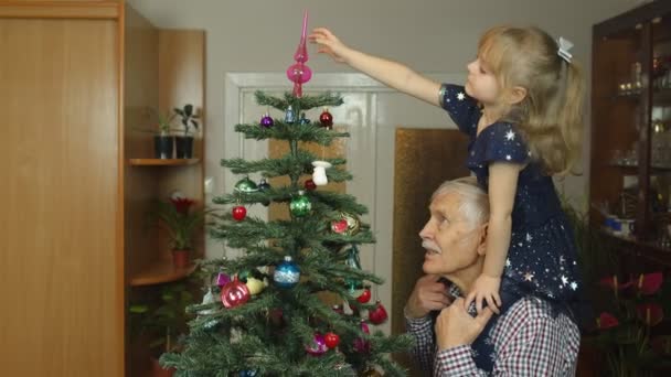 Menina criança e avô sênior decorando árvore de Natal artificial em casa, câmera lenta — Vídeo de Stock
