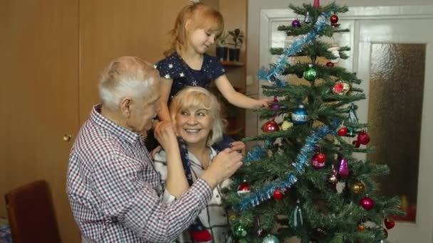 Kinderen meisje met grootouders paar versieren kunstmatige kerstboom in ouderwetse huis — Stockvideo