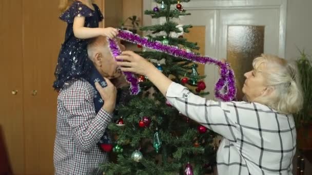 Mädchen mit Senioren-Oma, Opa schmückt künstlichen Weihnachtsbaum mit Ornamenten und Spielzeug — Stockvideo