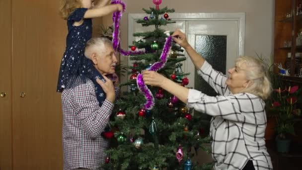 Niña con ancianos pareja abuelos decorando pino artificial de Navidad en casa — Vídeos de Stock