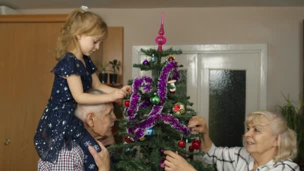 Kleine süße Mädchen mit Senioren Großeltern Familie schmücken künstlichen Weihnachtsbaum zu Hause — Stockvideo