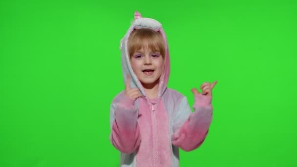 Маленькая блондинка девочка улыбается, танцует, празднует в пижаме единорога костюм на хрома ключ — стоковое видео