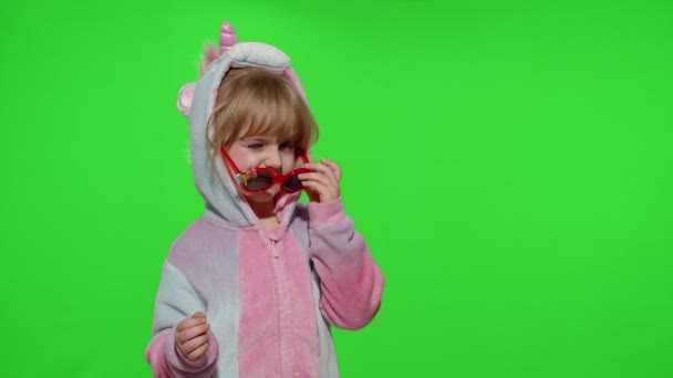 Маленькая девочка улыбается, танцует, подмигивает, празднует в пижаме единорога костюм на хрома ключ — стоковое видео